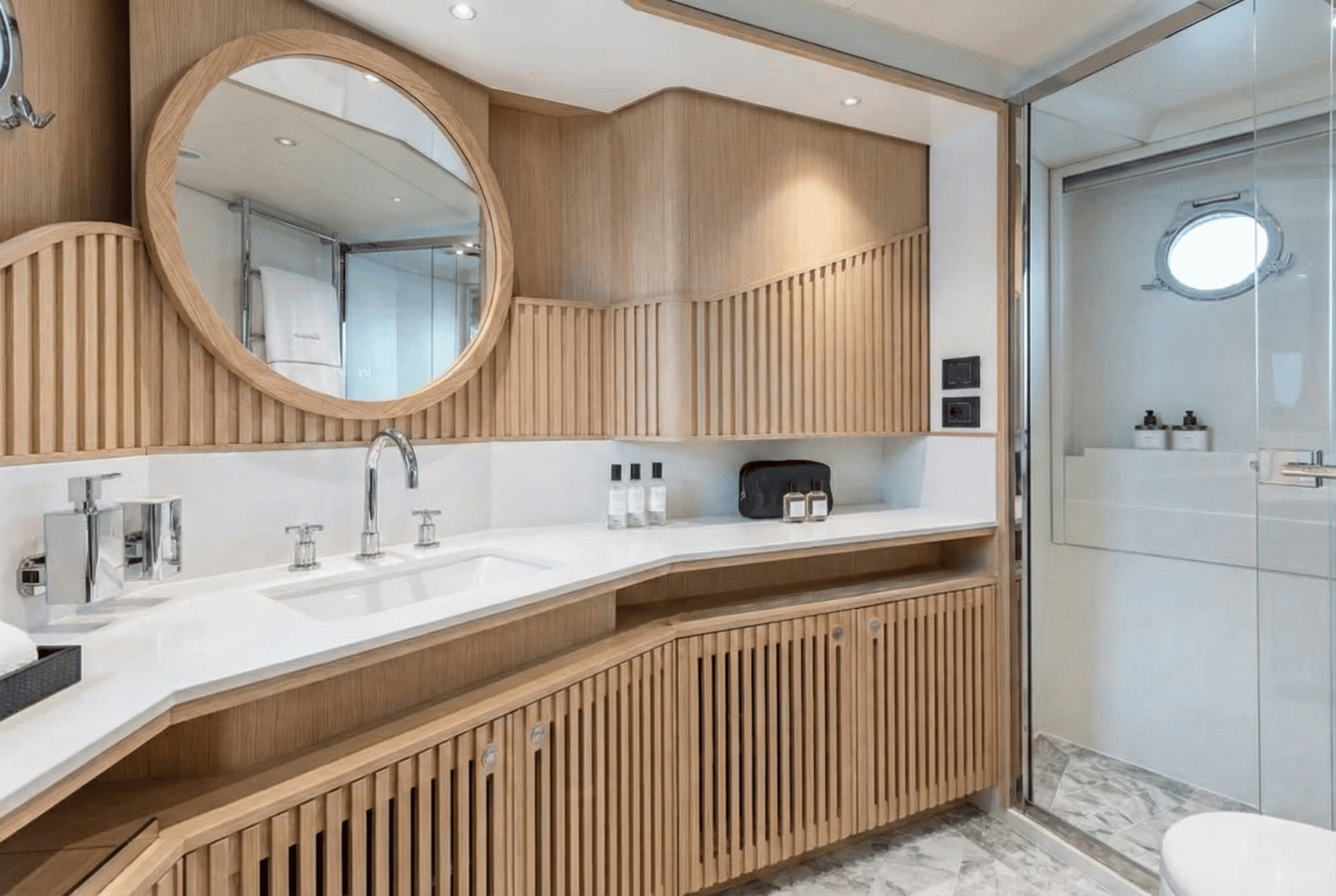 Modern marine bathroom featuring a slatted wood vanity and circular mirror. Premium yacht interior woodwork crafted for Victoria BC.